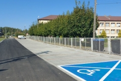 Miejsca parkingowe obok Szkoły w Rzuchowej. Na pierwszym planie wyznaczone miejsce dla osób z niepełnosprawnościami. Po lewej stronie parkingu nowa asfaltowa droga.