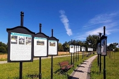 Wąska alejka z kostki brukowej pomiędzy tablicami historycznymi na tle błękitnego nieba