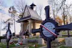 Metalowy krzyż nagrobny, przez środek nałożona biało-czerwona opaska