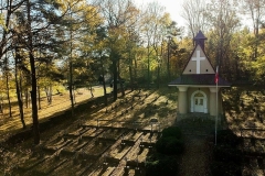 Kaplica cmentarna pomiędzy drzewami, wokoło mogiły żołnierskie