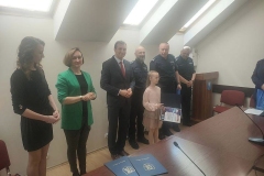 Dziecko trzyma dyplom i stoi obok komisji konkursowej