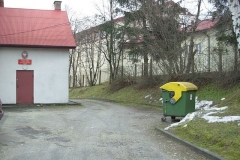 Wejście do posterunku dzielnicowych, z prawej zielony kosz na śmieci
