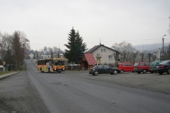 Autobus podjeżdżający na plac, na którym stoją zaparkowane samochody