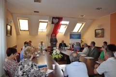 Wójt przemawia do zgromadzonych gości siedzących wokół stołu