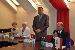 Wójt przemawia w pozycji stojącej, w tle biało-czerwona flaga