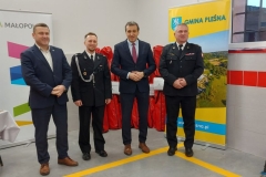 Wójt ze strażakami, w tle roll-upy województwa małopolskiego i Gminy Pleśna