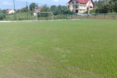 Zielona murawa na boisku, w tle biały budynek z czerwonym dachem