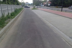 Wąska droga asfaltowa obok drogi głównej, z prawej strony czerwona kostka brukowa