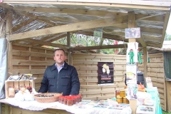 Mężczyzna przy stoisku z materiałami promocyjnymi, z tyłu drewniany prarawan