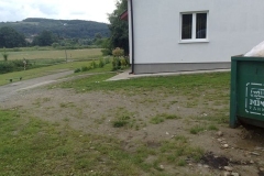 Boczna elewacja budynku z rynną, z prawej zielony kontener na śmieci