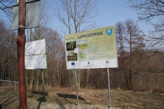 Tablica turystyczna w Łowczówku, za nią las