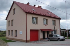 Różowy budynek remizy z czerwonym dachem i czerwoną bramą garażową