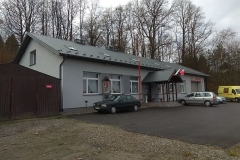 Niebieski budynek z zielonym dachem, przed budynkiem zaparkowane samochody