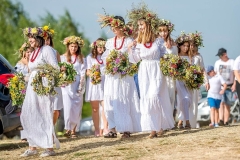 Dzieci ubrane w białe suknie z wiankami na głowach niosące bukiety z kwiatów i ziół