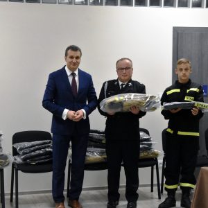 Wójt Józef Knapik przekazuje komplet ubrań specjalnych dwóm przedstawicielom OSP Rzuchowa