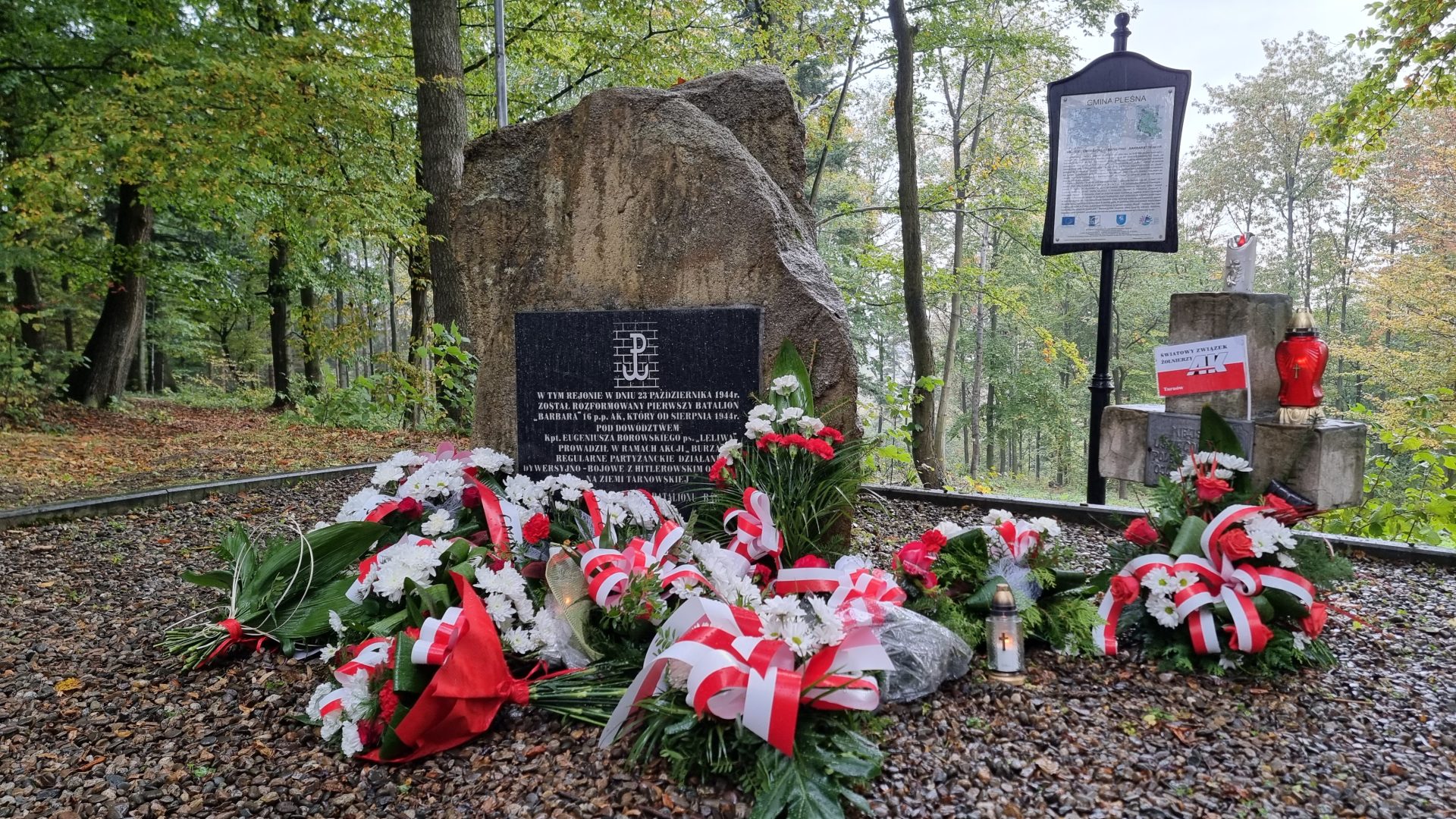 Zdjęcie przedstawia wiązanki kwiatów złożone przy obelisku upamiętniającym batalion AK "Barbara"