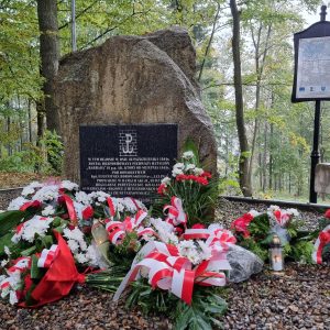 Zdjęcie przedstawia wiązanki kwiatów złożone przy obelisku upamiętniającym batalion AK "Barbara"