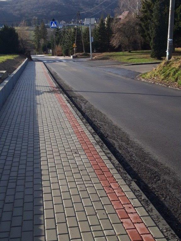 Fragment drogi asfaltowej, w dali przejście dla pieszych, z lewej strony chodnik z kostki brukowej