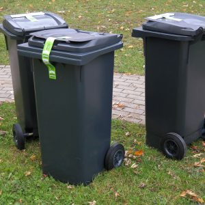 Trzy czarne kosze na śmieci stojące na trawniku