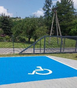 Miejsce parkingowe - prostokąt wymalowany na niebiesko. W środku prostokąta symbol osoby siedzącej na wózku.