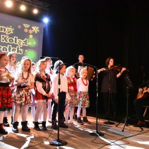 Grupa dzieci w strojach regionalnych śpiewa na scenie.