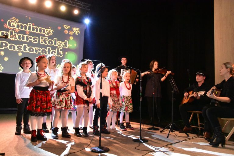 Grupa dzieci w strojach regionalnych śpiewa na scenie.