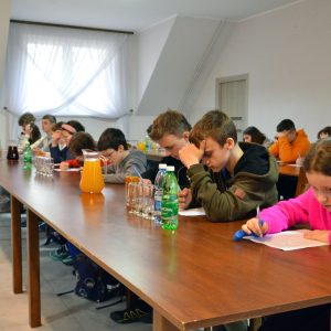 Na zdjęciu dzieci siedzą przy stołach, w rękach trzymają długopisy i rozwiązują test.