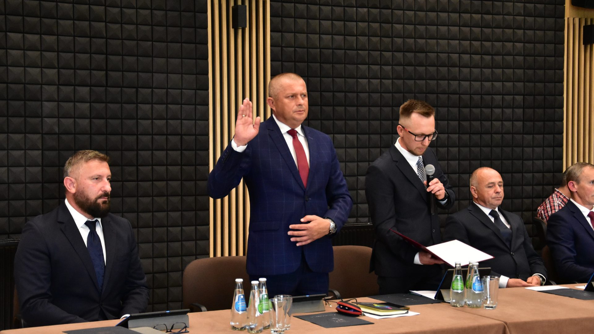 Na zdjęciu czterech mężczyzn. Jeden z nich unosi prawą rękę w górę i składa ślubowanie.