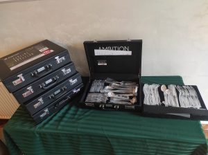 Na zdjęciu czarne walizki poukładane na stole. Na środku blatu jedna z walizek jest otwarta.