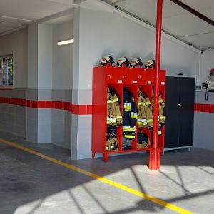 Wnętrze garażu OSP Szczepanowice, widok na białe ściany, w środku czerwone szafki ze strojami roboczymi
