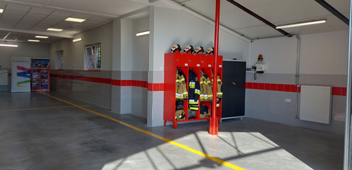 Wnętrze garażu OSP Szczepanowice, widok na białe ściany, w środku czerwone szafki ze strojami roboczymi