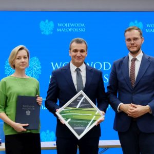 Stoją od lewej: Joanna Krochmal Skarbnik Gminy Pleśna, Józef Knapik Wójt Gminy Pleśna, Łukasz Krzysztofik Dyrektor Biura Wojewody. Pani Skarbnik trzyma w rękach umowę dofinansowania. Pan Wójt trzyma w rękach nagrodę - znak bezpiecznych inwestycji dla Gminy Pleśna.