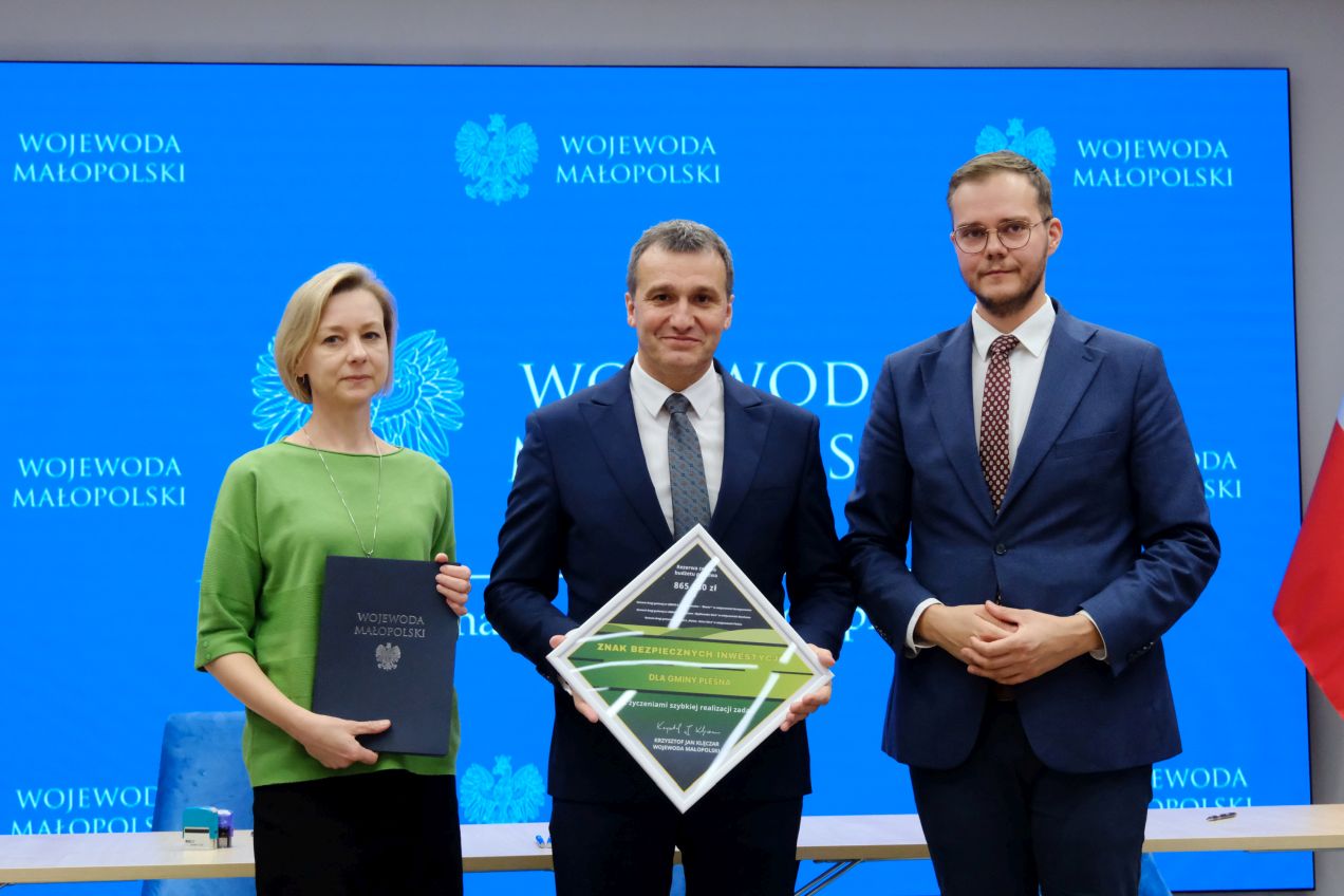 Stoją od lewej: Joanna Krochmal Skarbnik Gminy Pleśna, Józef Knapik Wójt Gminy Pleśna, Łukasz Krzysztofik Dyrektor Biura Wojewody. Pani Skarbnik trzyma w rękach umowę dofinansowania. Pan Wójt trzyma w rękach nagrodę - znak bezpiecznych inwestycji dla Gminy Pleśna.