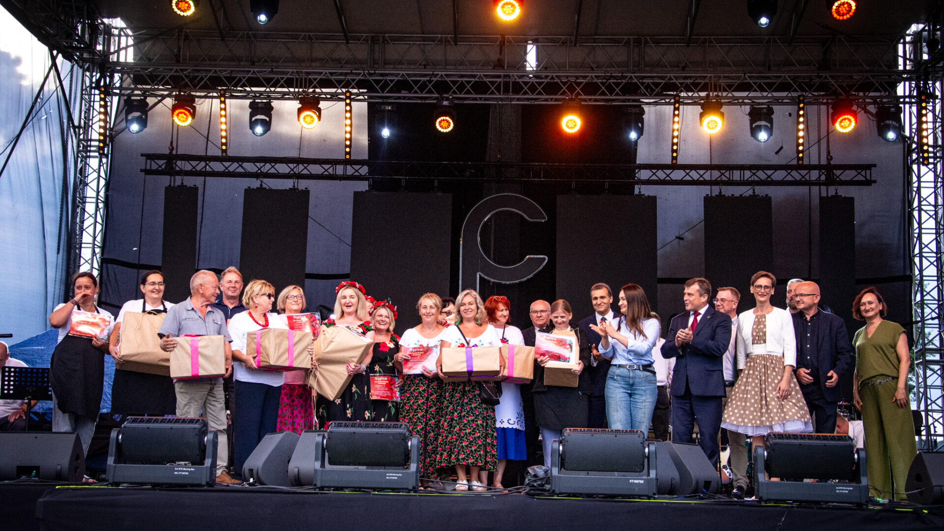 Osoby stojące w jednym rzędzie na scenie. Część z nich trzyma w dłoniach prezenty.