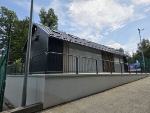Odnowiony budynek szatni. Przed budynkiem barierki.