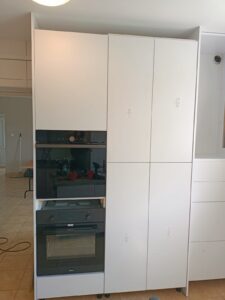 Dwa piekarniki w zabudowie oraz szafki w pomieszczeniu kuchennym