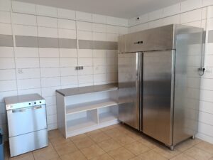 Chłodnia, półki i zmywarka ustawione w narożniku pomieszczenia kuchennego