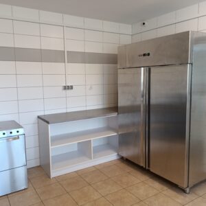 Chłodnia, półki i zmywarka ustawione w narożniku pomieszczenia kuchennego