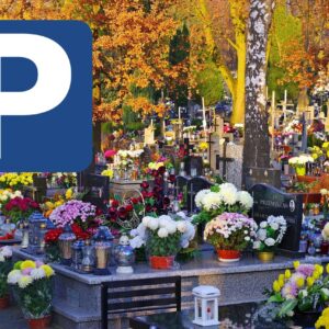 Fragment cmentarza, na nagrobkach znicze i kwiaty, z lewej znak informujący o parkingu