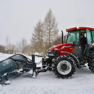 Traktor z zapiętym pługiem śnieżnym odgarnia śnieg