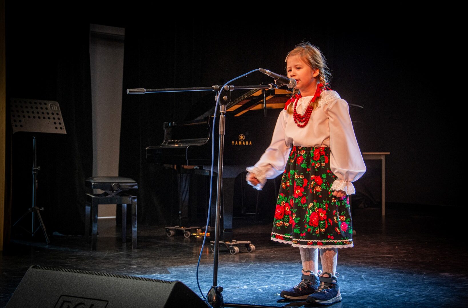 Dziewczynka w stroju krakowskim śpiewa do mikrofonu.