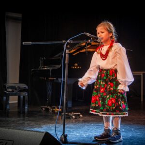 Dziewczynka w stroju krakowskim śpiewa do mikrofonu.