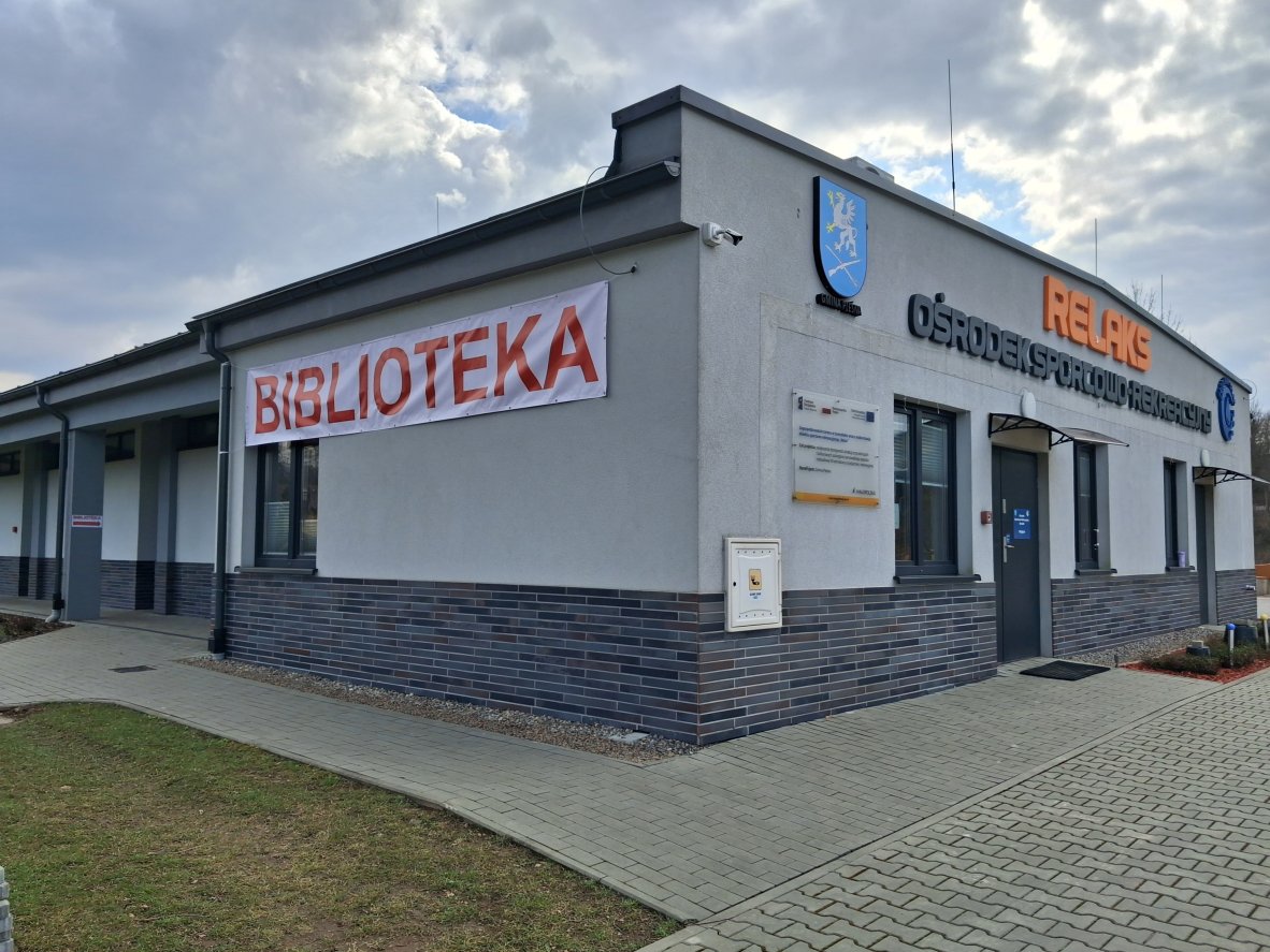 Wejście do budynku ośrodka Relaks, na ścianie wywieszony czerwony napis "biblioteka"