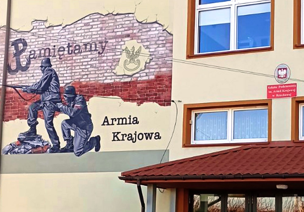 Fragment ściany placówki oświatowej z widocznym muralem przedstawiającym żołnierzy Armii Krajowej.