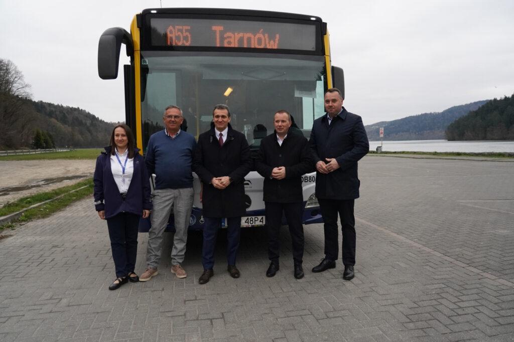 Czterech mężczyzn i jedna kobieta pozują do zdjęcia przed przodem autobusu.