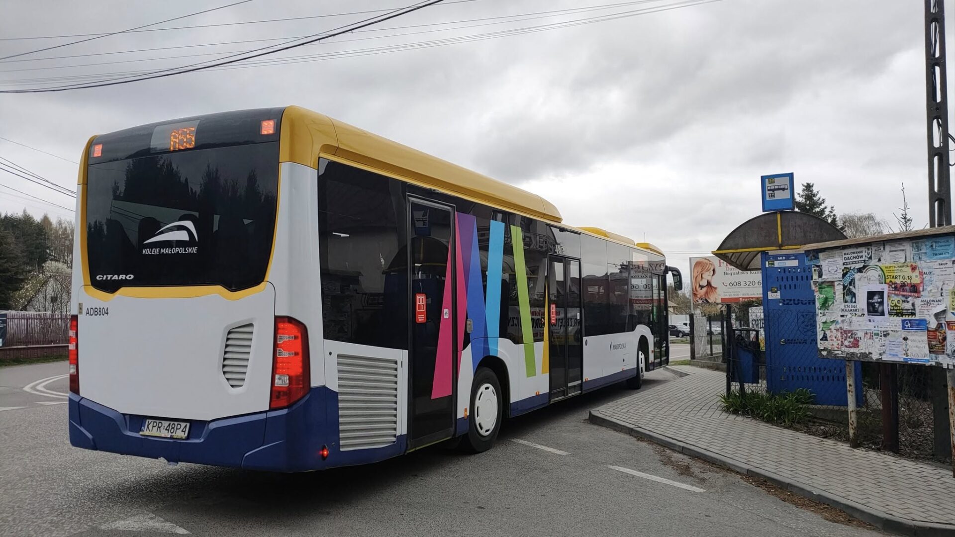 Wielokolorowy autobus stoi na zatoce autobusowej. Po prawej wiata przystankowa.