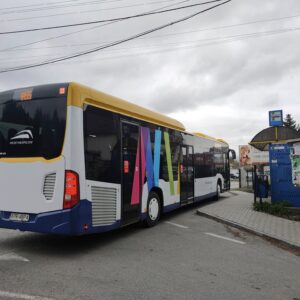 Wielokolorowy autobus stoi na zatoce autobusowej. Po prawej wiata przystankowa.