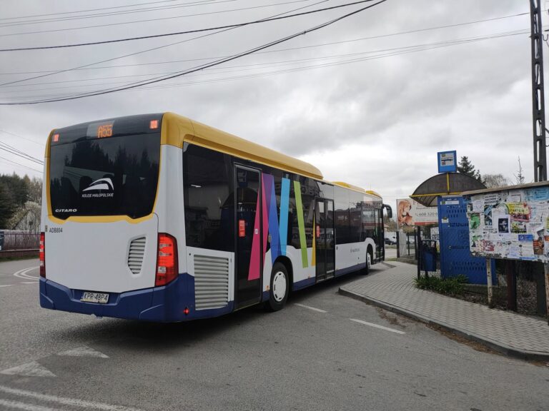 Wielokolorowy autobus stoi na zatoce autobusowej. Po prawej wiata przystankowa.