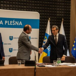 Na zdjęciu cztery osoby przy stole prezydialnym, dwie podają sobie ręce.