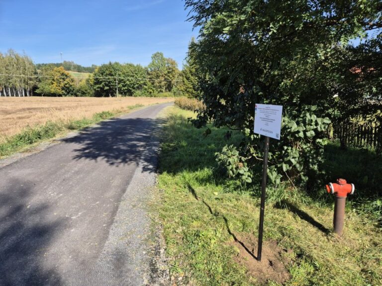 Nowa nakładka asfaltowa na drodze, z prawej strony znak informujący o dofinansowaniu i hydrant